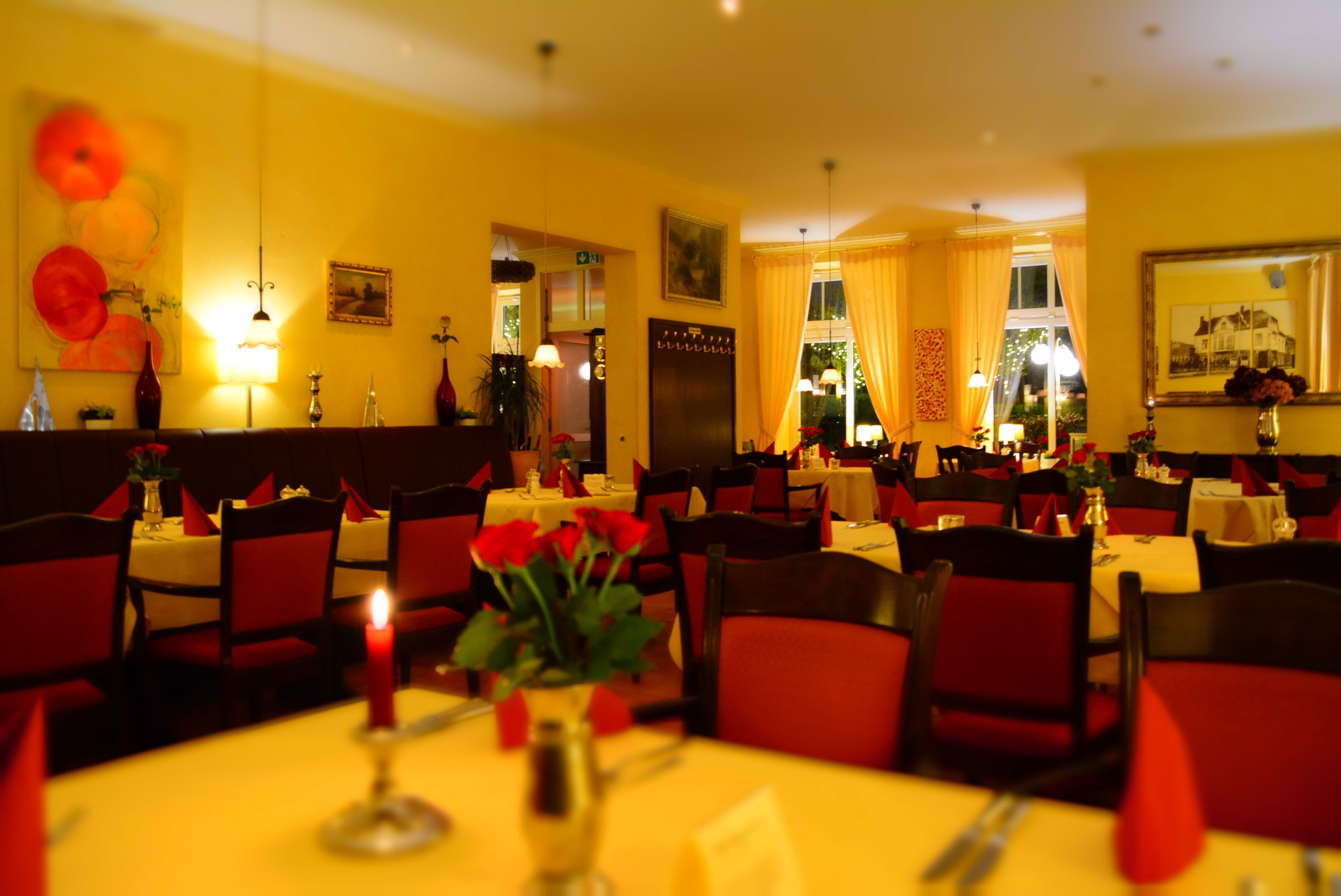 Een restaurant met meerdere tafels, rode stoelen en gele tafelkleden.