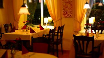 A dining area with tables set for two, chairs, and table lamps.