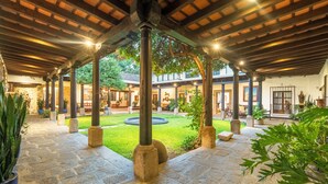 A covered courtyard with stone flooring, columns, and potted plants.