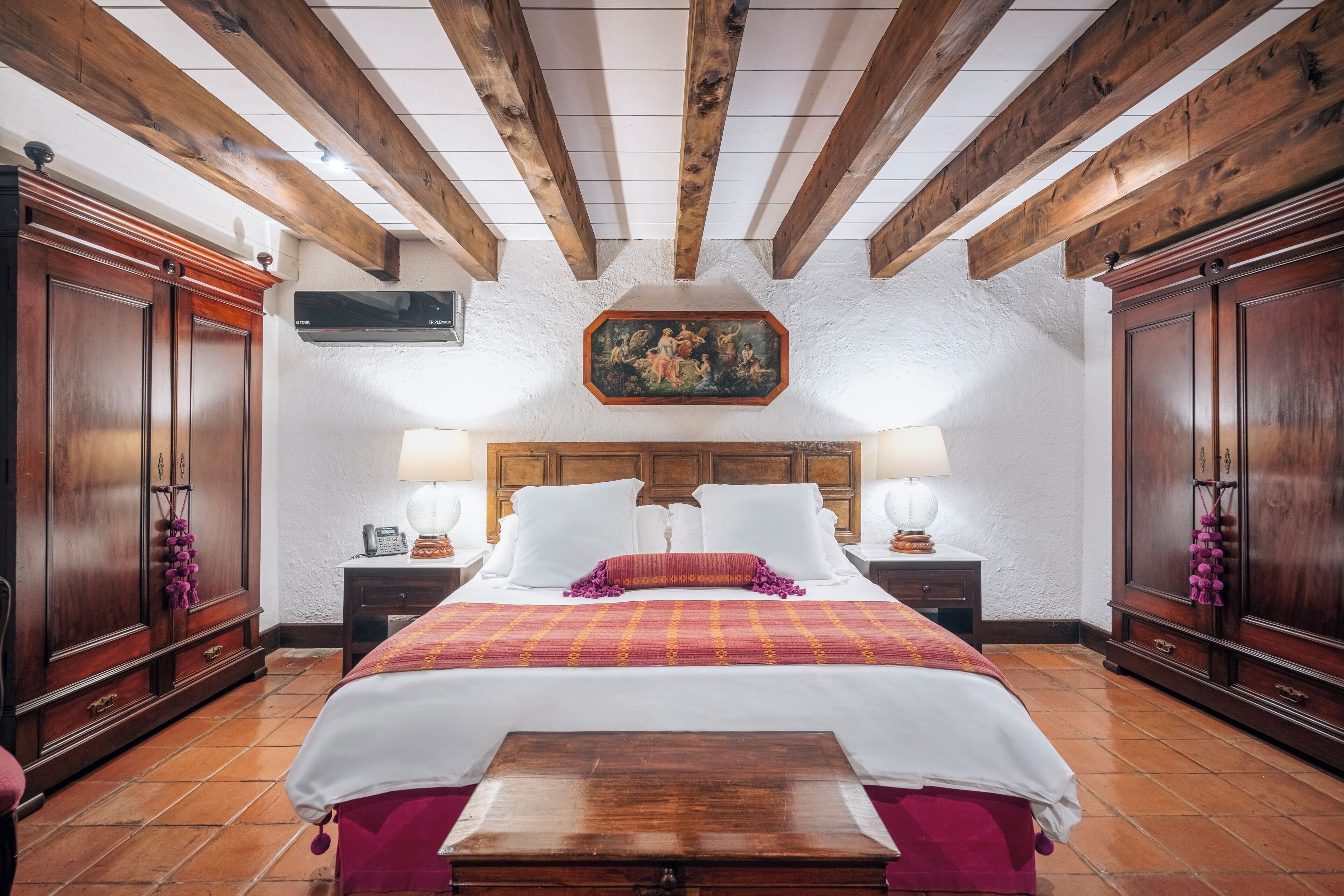 Ein Hotelzimmer mit Holzboden, einem großen Bett mit weißer und roter Bettwäsche, zwei Nachttischen und Holzschränken.
