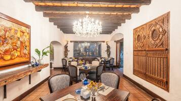 A dining area with wooden tables, chairs, a chandelier, and a large decorative panel on the wall.
