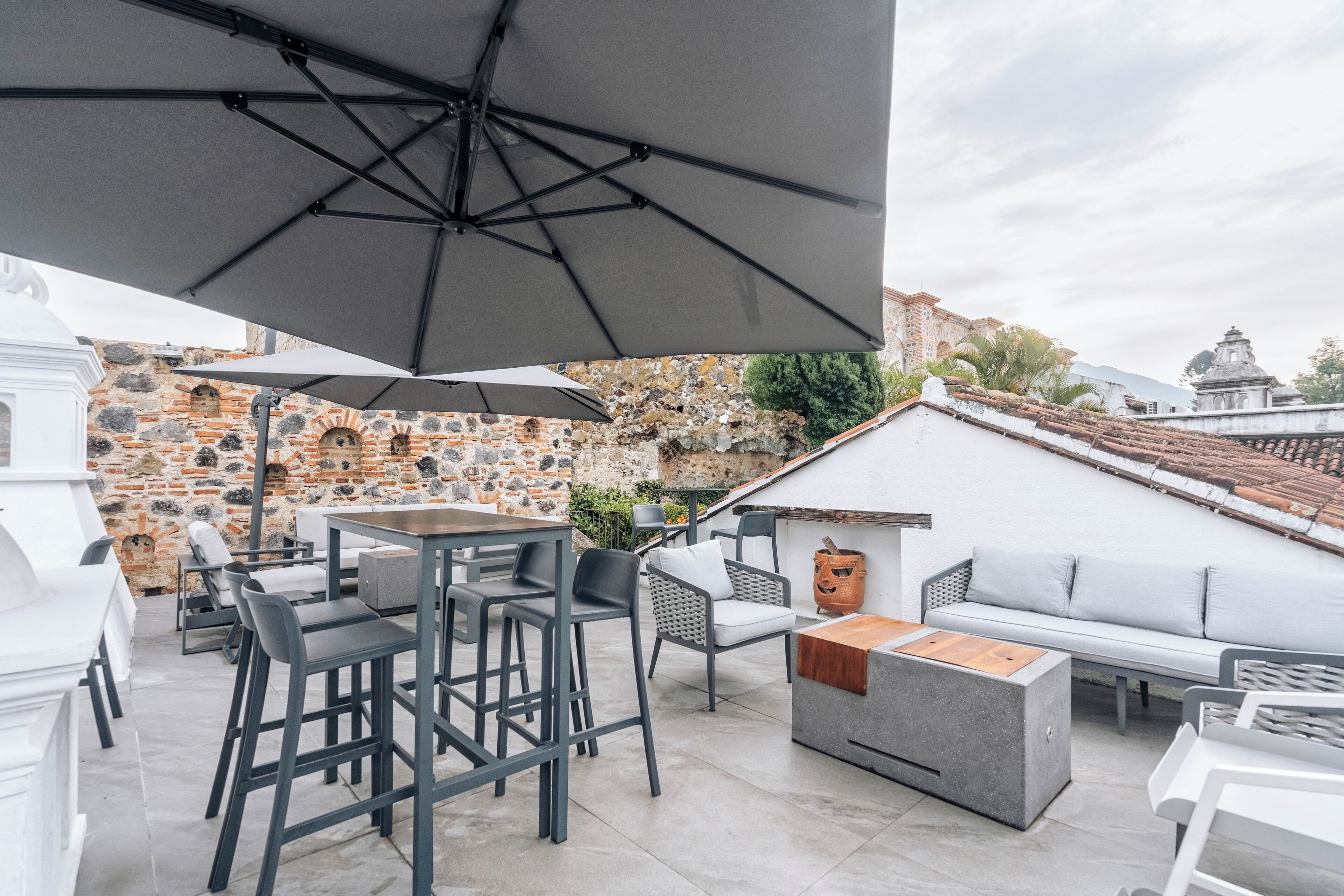 An outdoor patio with modern furniture, including bar stools and a sofa, under large umbrellas.