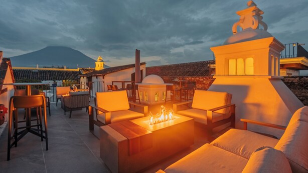 A rooftop terrace with outdoor seating, a fire feature, and a view of a mountain.