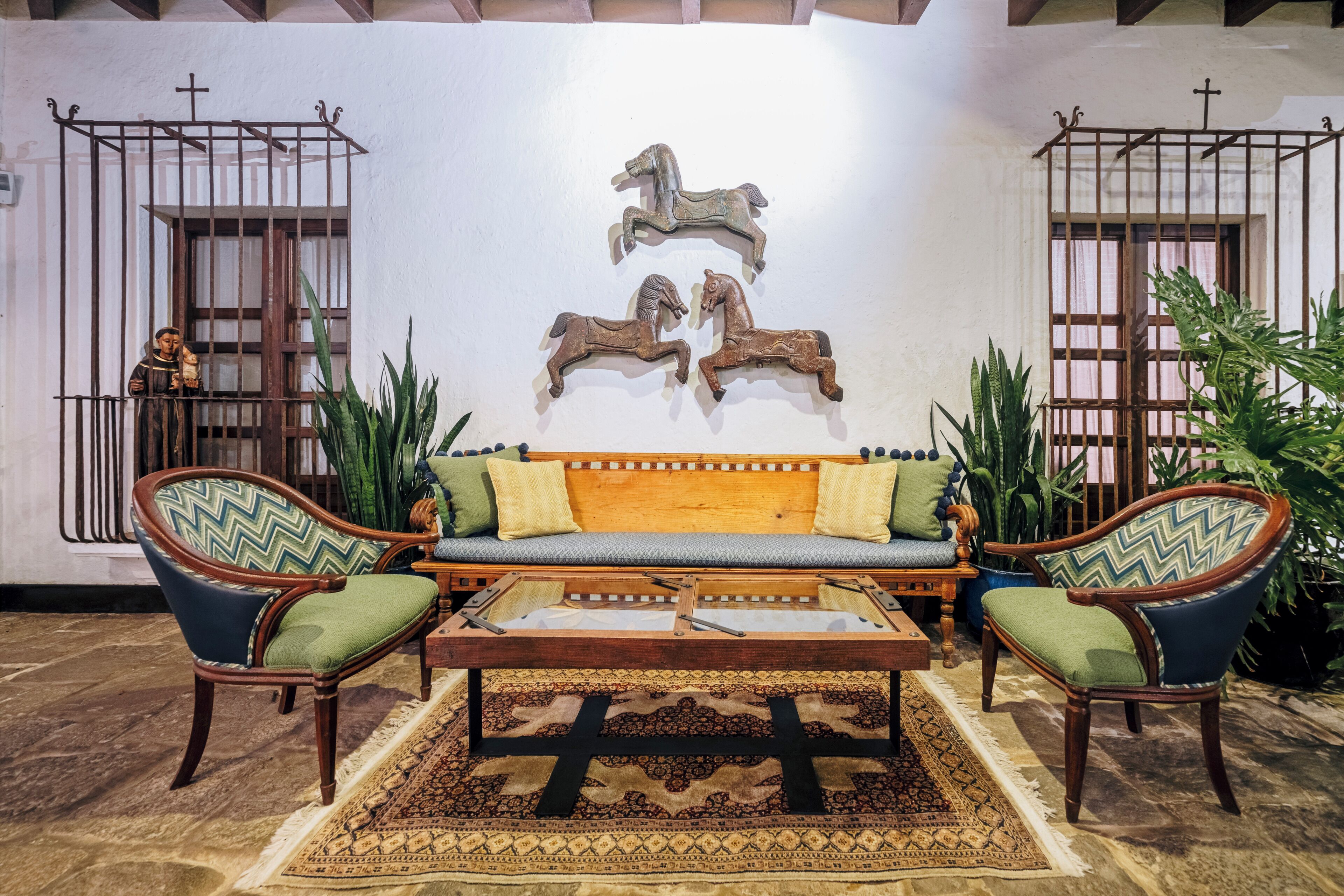 Una habitación con un sofá de madera, dos sillones, una mesa de centro y esculturas decorativas de caballos en la pared.