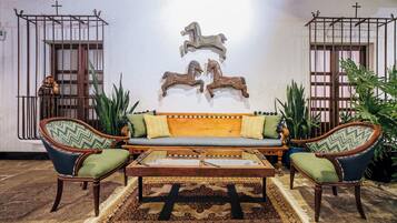 Una habitación con un sofá de madera, dos sillones, una mesa de centro y esculturas decorativas de caballos en la pared.
