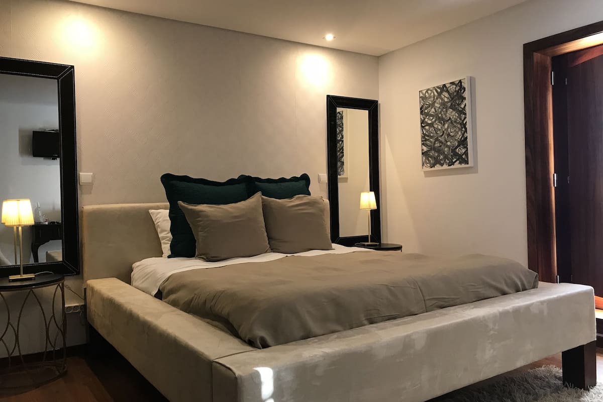 A modern bedroom with a large bed, two bedside tables with lamps, a large mirror, and a piece of abstract art on the wall.