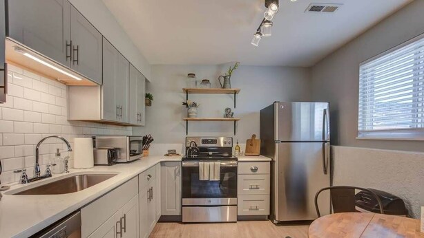 A modern kitchen with stainless steel appliances, white cabinetry, and a wooden dining table. - Steps to Red Rocks Trails by Old Colorado City Pad (Colorado Springs)