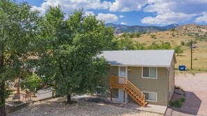 A single-story building with a wooden staircase leading to a door, surrounded by gravel and trees. - Steps to Red Rocks Trails by Old Colorado City Pad (Colorado Springs)