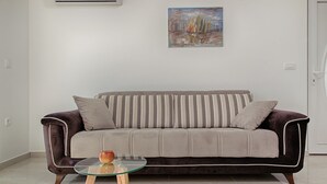 A modern living room with a grey sofa, striped cushions, a glass coffee table with an apple, and a painting of sailboats on the wall. - Cezar Luxury Apartments (Omis)