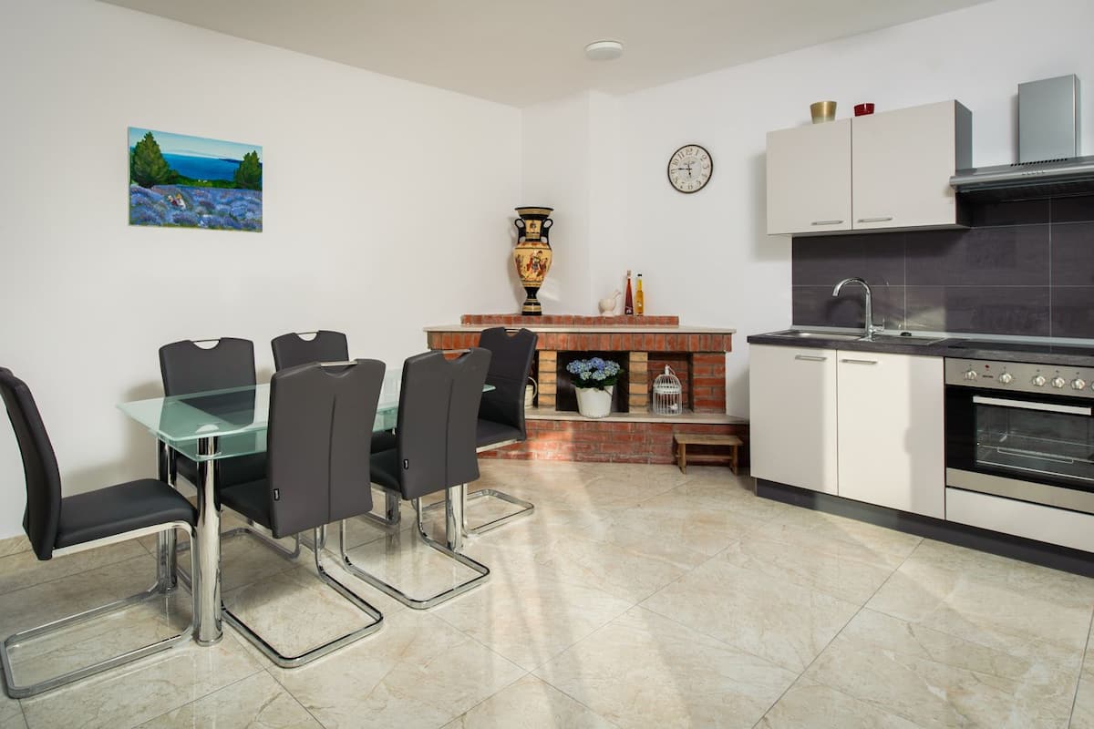 A modern kitchen with a dining area, featuring a glass table, black chairs, a brick fireplace, and a built-in oven.