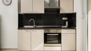 A modern kitchen with a stainless steel sink, a built-in oven, and a gas stove. There is a clock on the wall and a window providing natural light. - Cezar Luxury Apartments (Omis)