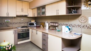Una cocina moderna con electrodomésticos de acero inoxidable, un microondas y un hervidor. Hay armarios con manijas y un estante pequeño con objetos decorativos.