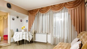Una sala de estar con un sofá, una mesa de comedor con sillas, un radiador y cortinas.