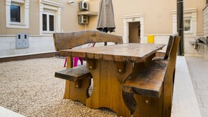 Una mesa de madera y bancos en un patio exterior con un edificio al fondo.