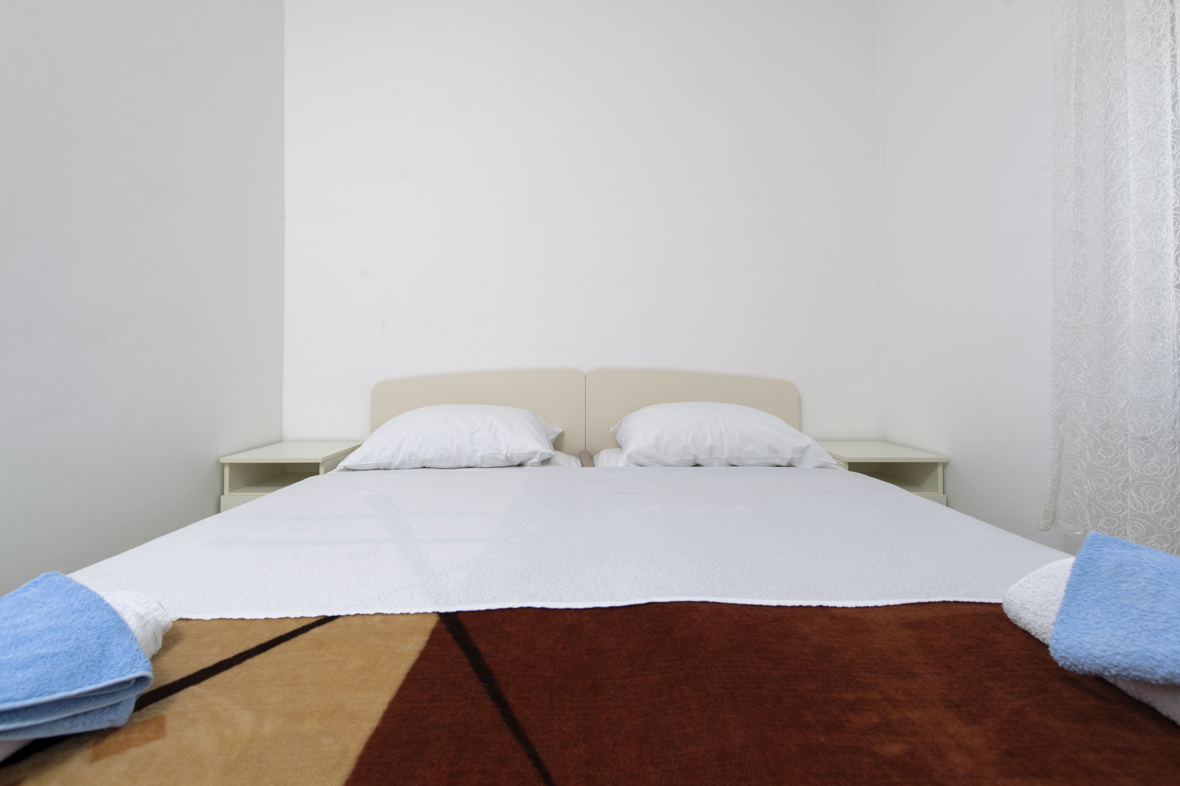 Una cama doble con sábanas blancas, un tapete marrón y dos almohadas blancas.