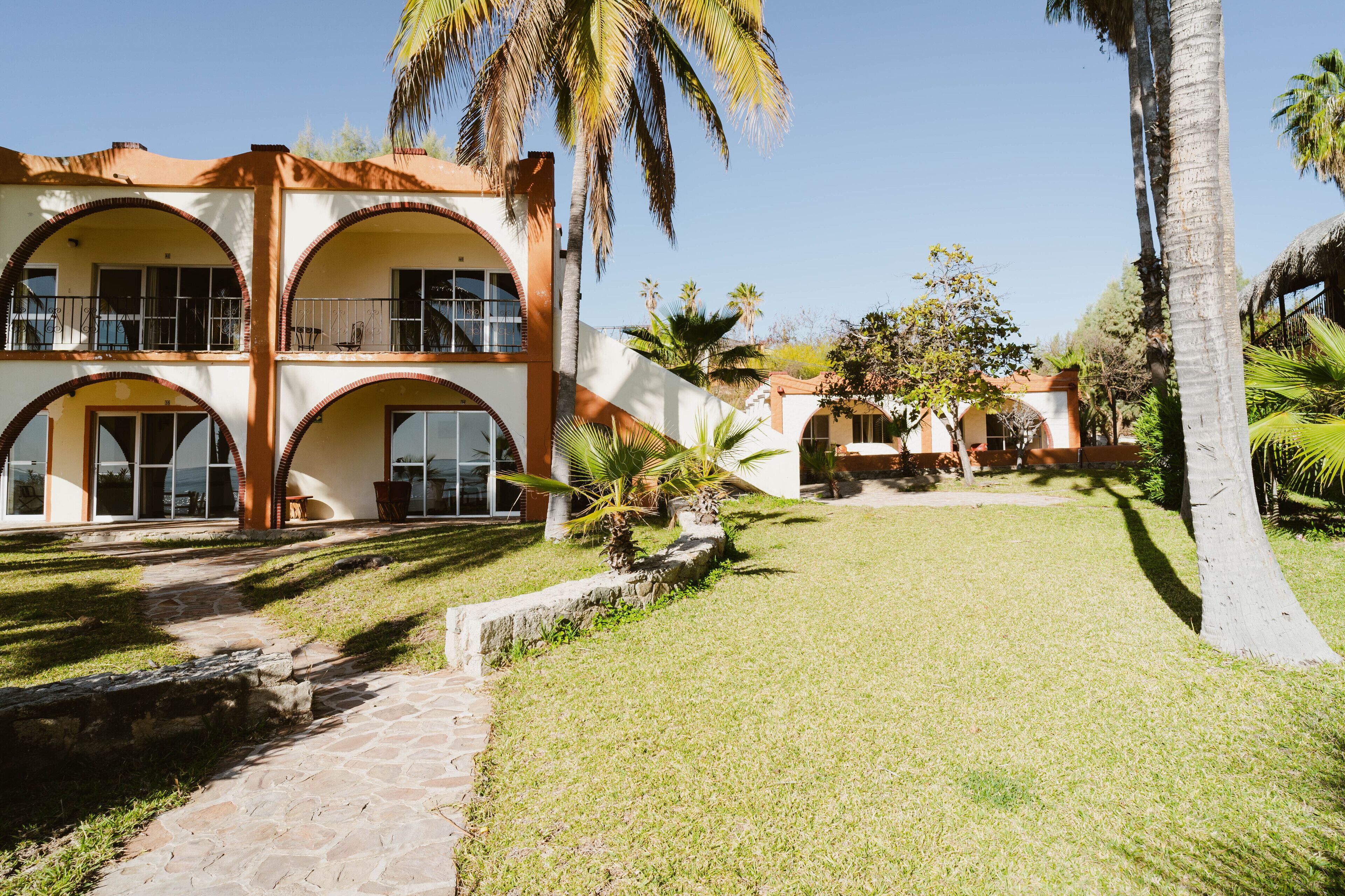 Un edificio de dos plantas con un patio central, rodeado de palmeras y un sendero de piedra.