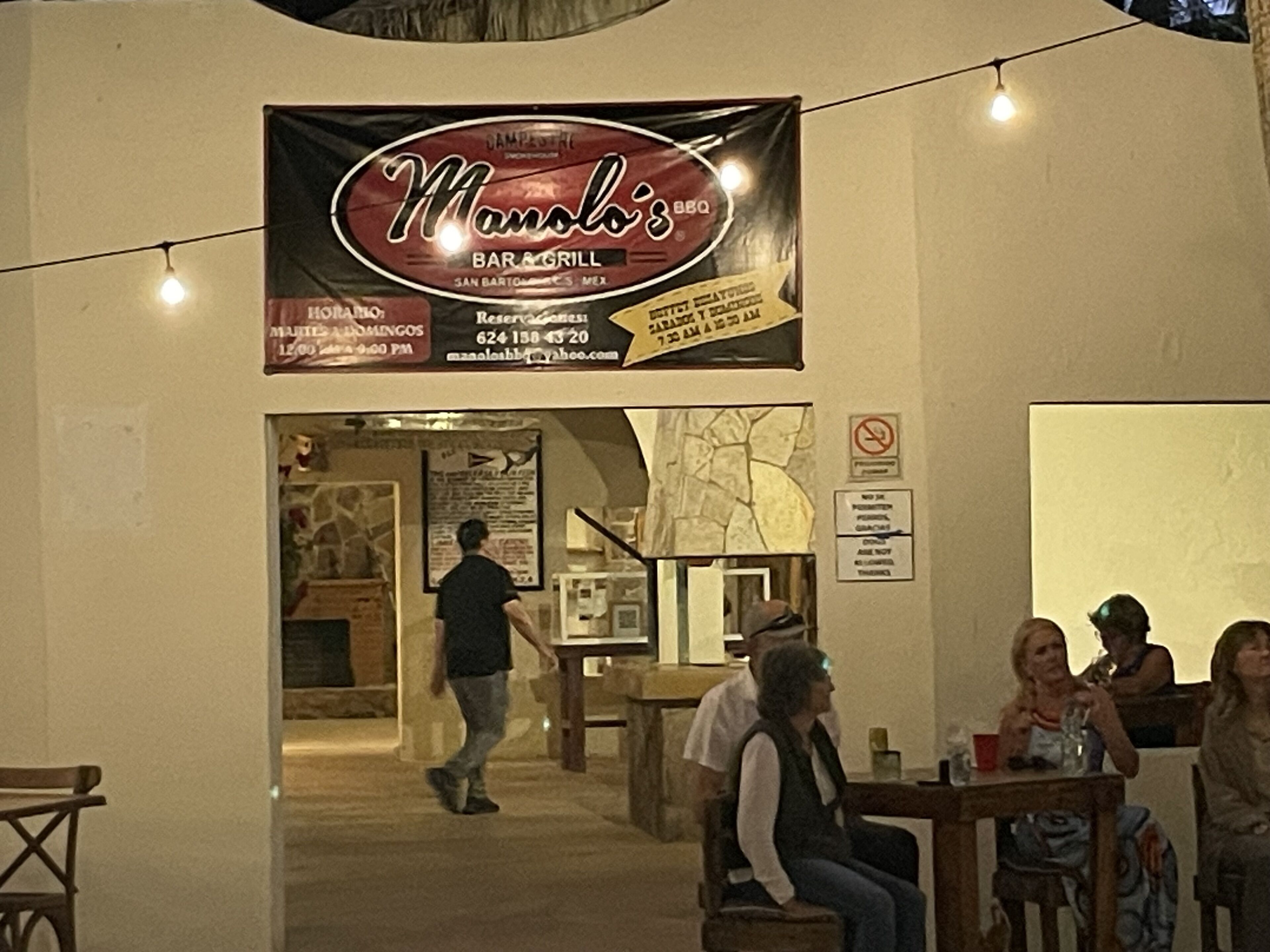 Un restaurante llamado Manolo's Bar & Grill con un cartel que indica que está abierto para el almuerzo y la cena.