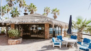 A covered outdoor seating area with stone flooring, blue-striped chairs, and a thatched roof. - Hotel Rancho Buena Vista (Buenavista)