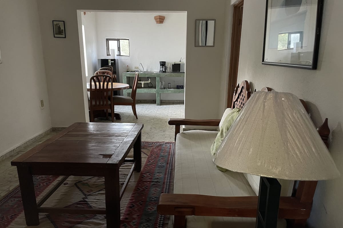 Ein Essbereich mit Holztisch und -stühlen, eine Couch mit einem gemusterten Teppich und eine Küche im Hintergrund.