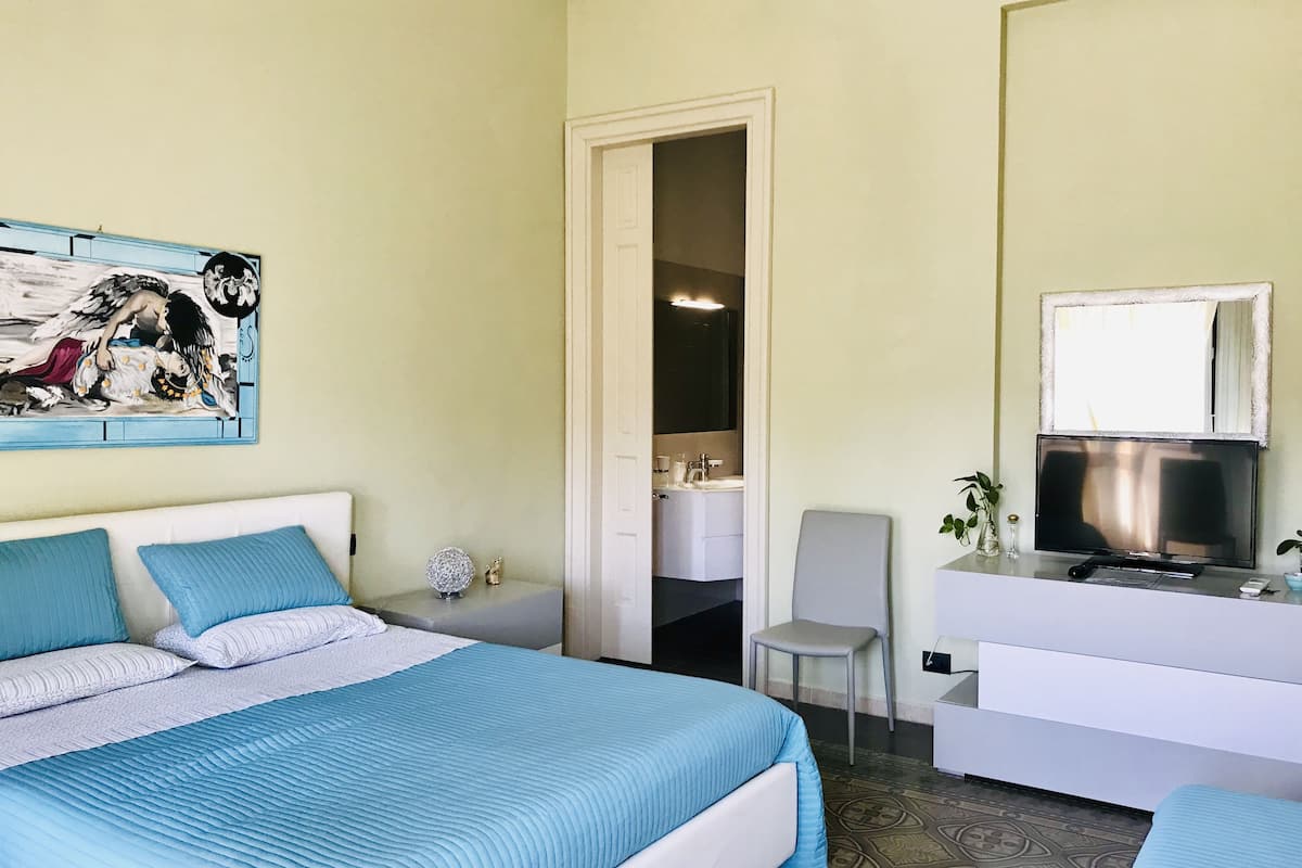 Une chambre à coucher avec un lit, un bureau, une chaise et une salle de bain visible à travers une porte ouverte.
