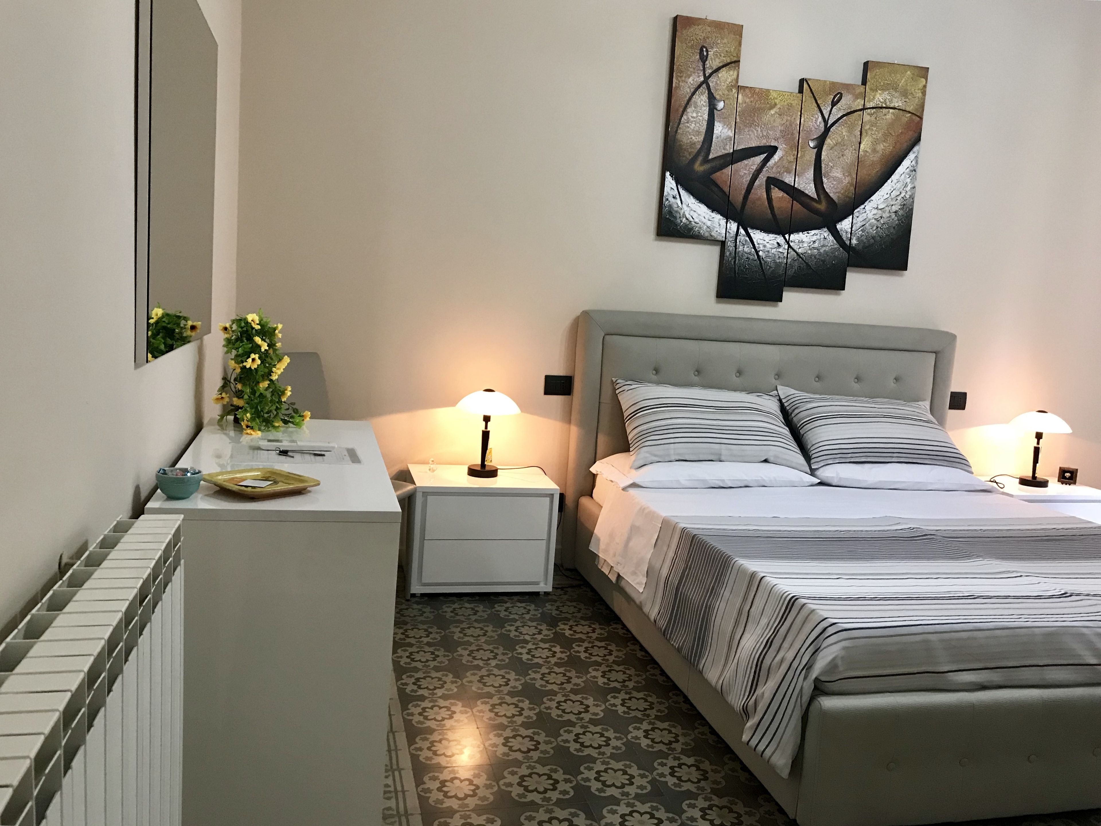 A neatly arranged bedroom with a bed, bedside tables, a desk, and a large abstract painting on the wall.