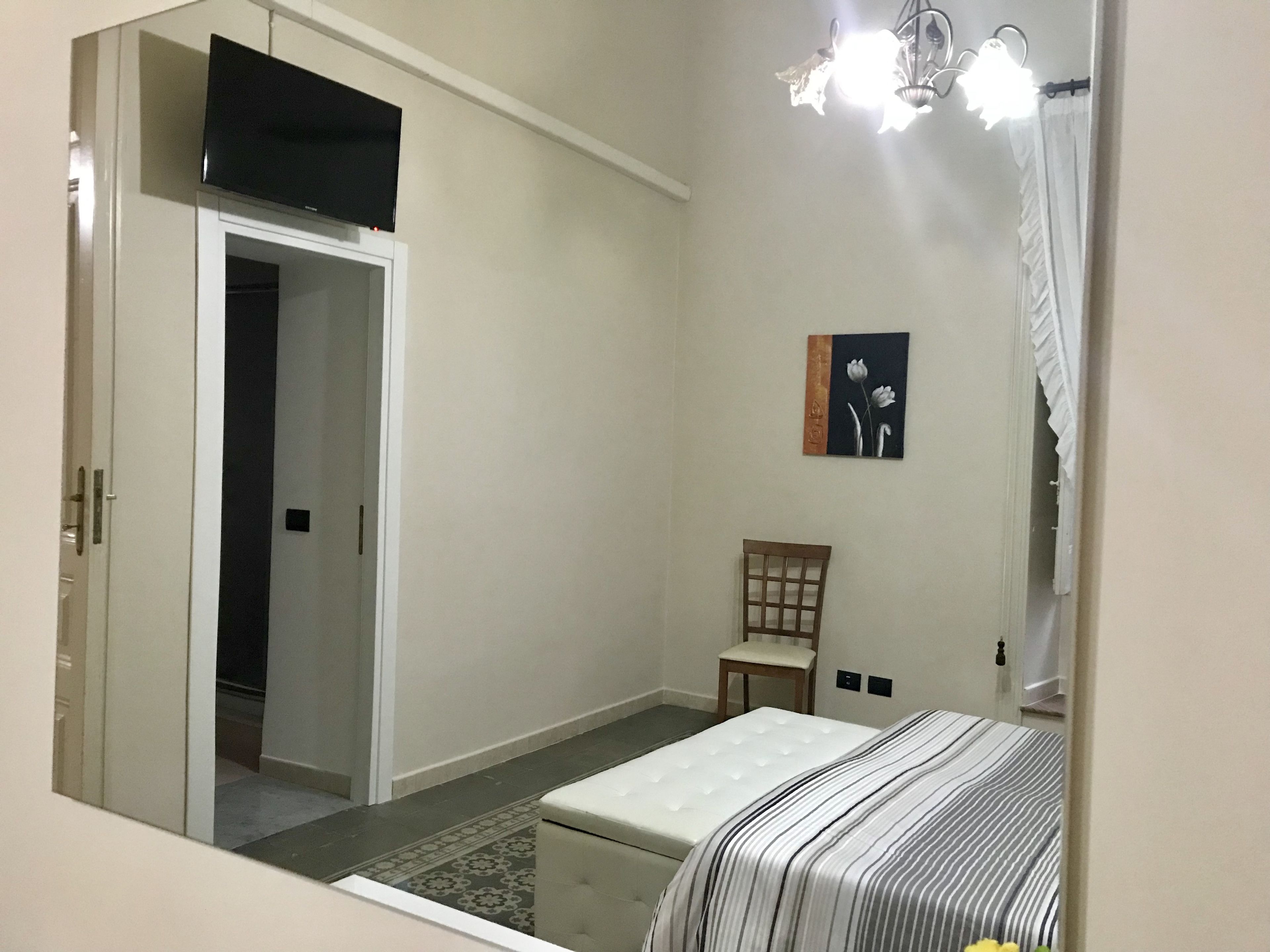 A bedroom with a bed, a chair, a painting, and a television on the wall.