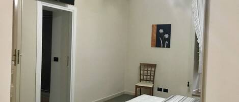 A bedroom with a bed, a chair, a painting, and a television on the wall.
