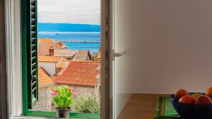 Una ventana con vistas a un pueblo costero, una planta en maceta y un frutero sobre una mesa.