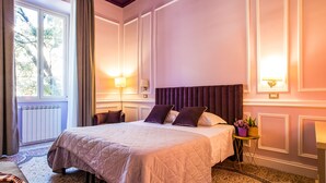 A hotel room with a large bed, two bedside lamps, a small table with a plant, and a window with curtains. - Hold Rome (Rome)