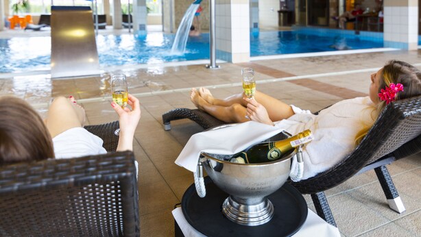 Un espace aménagé au bord de la piscine, avec des chaises longues, une bouteille de champagne et un verre de champagne.