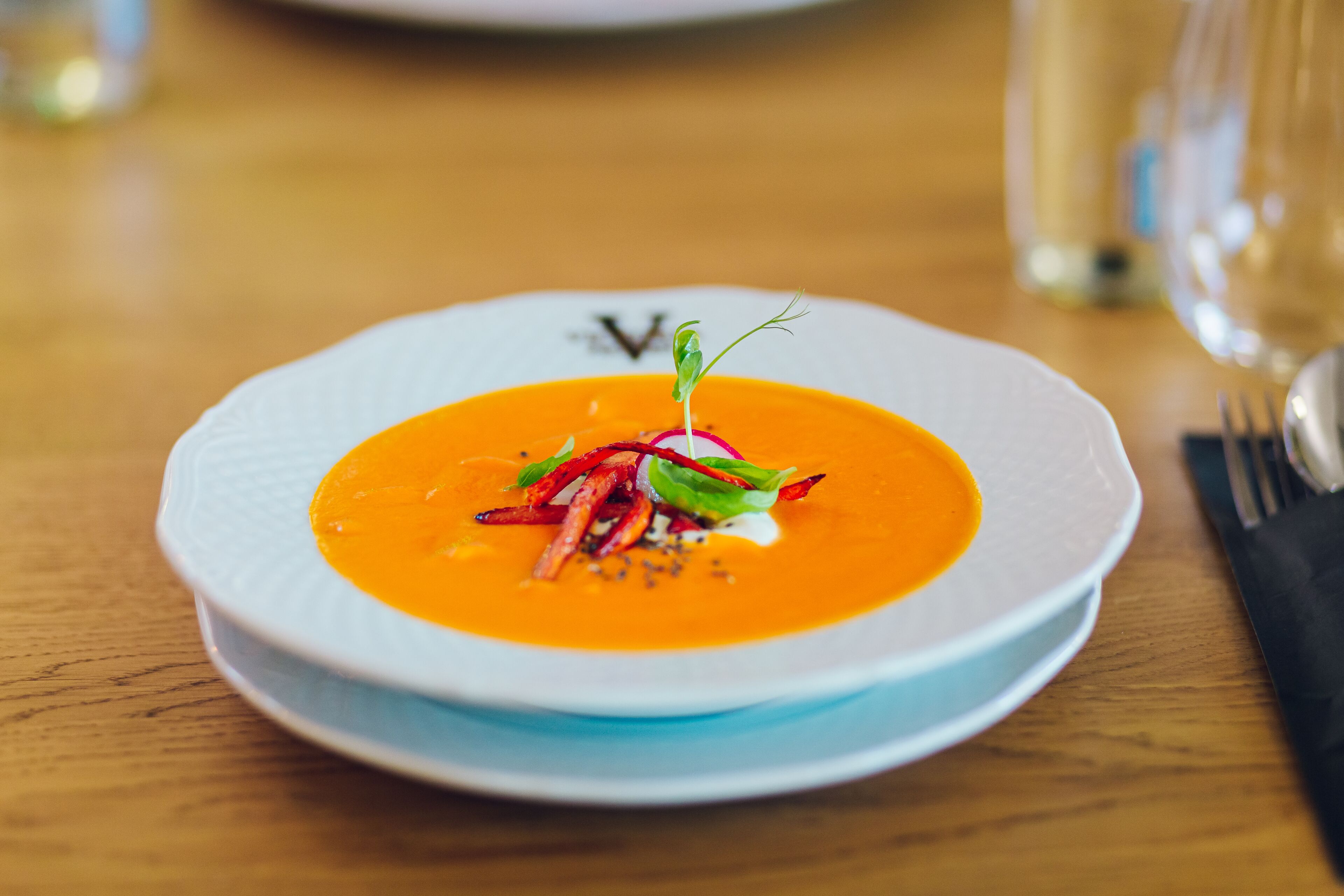 A white plate with a bowl of soup garnished with greens and a sprig of herb.