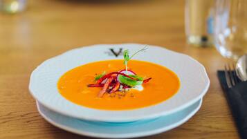 A white plate with a bowl of soup garnished with greens and a sprig of herb.