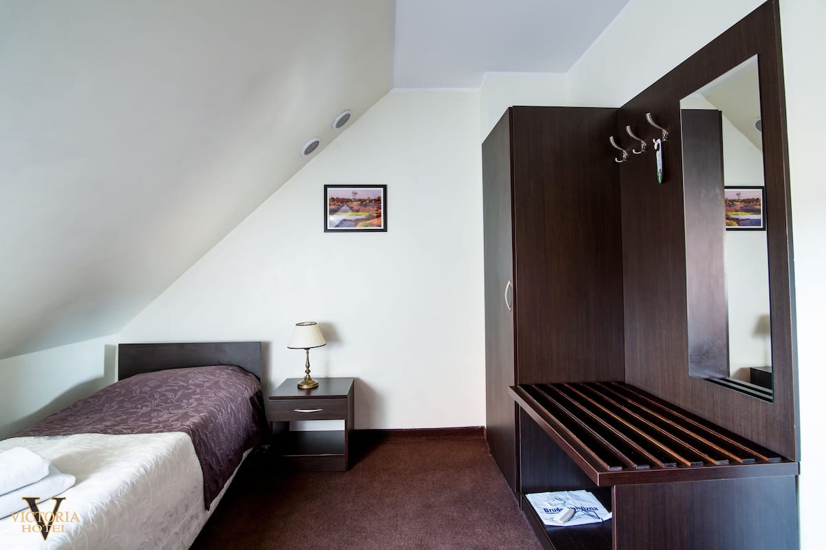 A bedroom with a bed, a nightstand, a lamp, a wardrobe, and a picture on the wall.