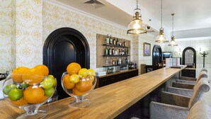 Un espace bar avec un long comptoir en bois, deux bols en verre remplis de fruits et un mur recouvert d’étagères à bouteilles.