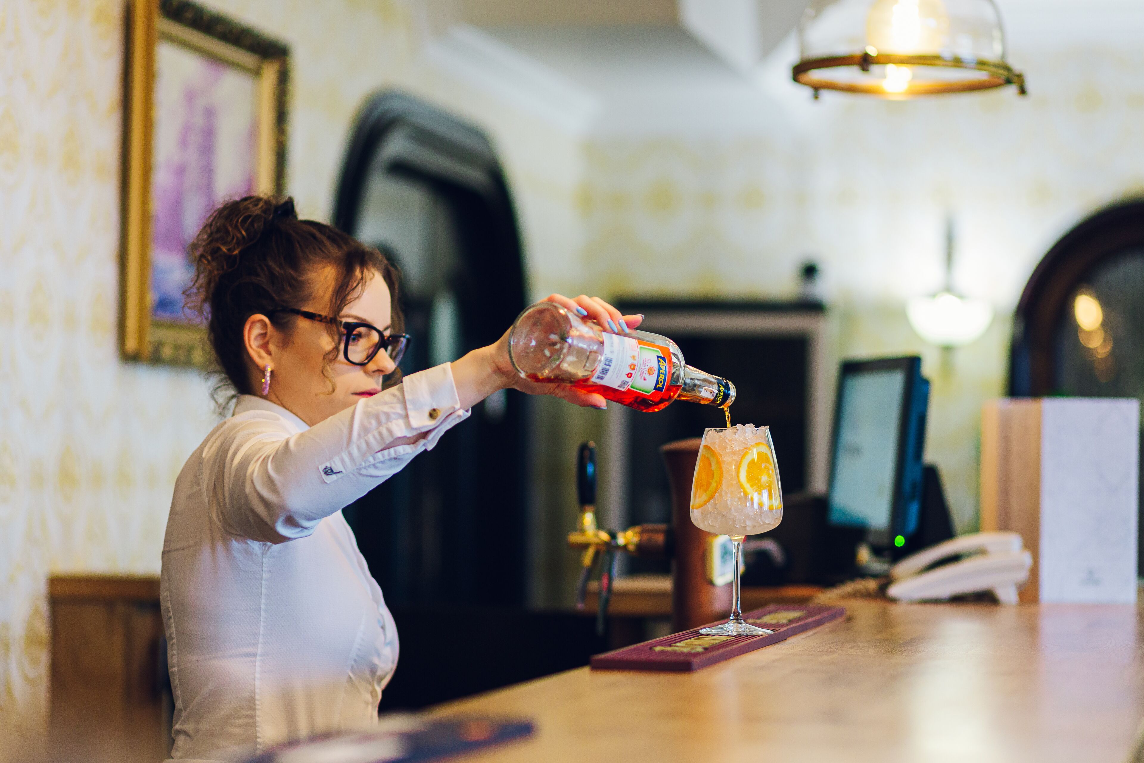 Um bartender servindo uma bebida em um copo com gelo e uma fatia de laranja.
