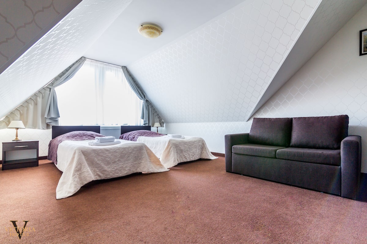 A hotel room with two beds, a sofa, a lamp, and a large window.