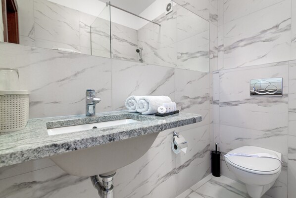 Un baño moderno con lavamanos de mármol, inodoro y zona de ducha.