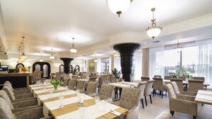 Un vaste espace dédié à la salle à manger, avec de nombreuses tables et chaises, de grandes fenêtres et de magnifiques lustres.