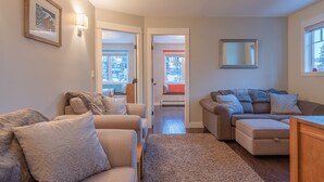 A cozy living room with two sofas, a coffee table, and a rug. There are two windows with views of a snowy landscape. - Main House on Knoll - semi-private hot tub, pet friendly, BBQ, near trails (Silver Star Mountain)