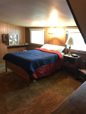 A bedroom with a bed, a bedside table with a lamp, a window, and a small desk with a chair. - Vintage 1950's Lakefront Cabin  Private Dock, Sunrise Views & Pet Friendly (Lakeville)