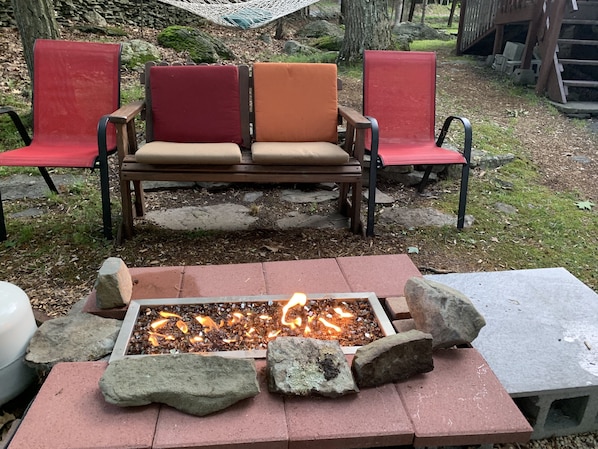 Un foyer extérieur entouré de pierres et un banc agrémenté de coussins rouges et orange.
