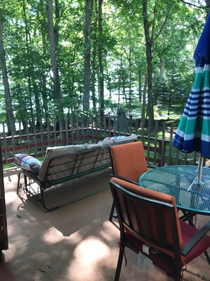 An outdoor patio area with a metal table and chairs, a cushioned bench, and a striped umbrella. - Vintage 1950's Lakefront Cabin  Private Dock, Sunrise Views & Pet Friendly (Lakeville)