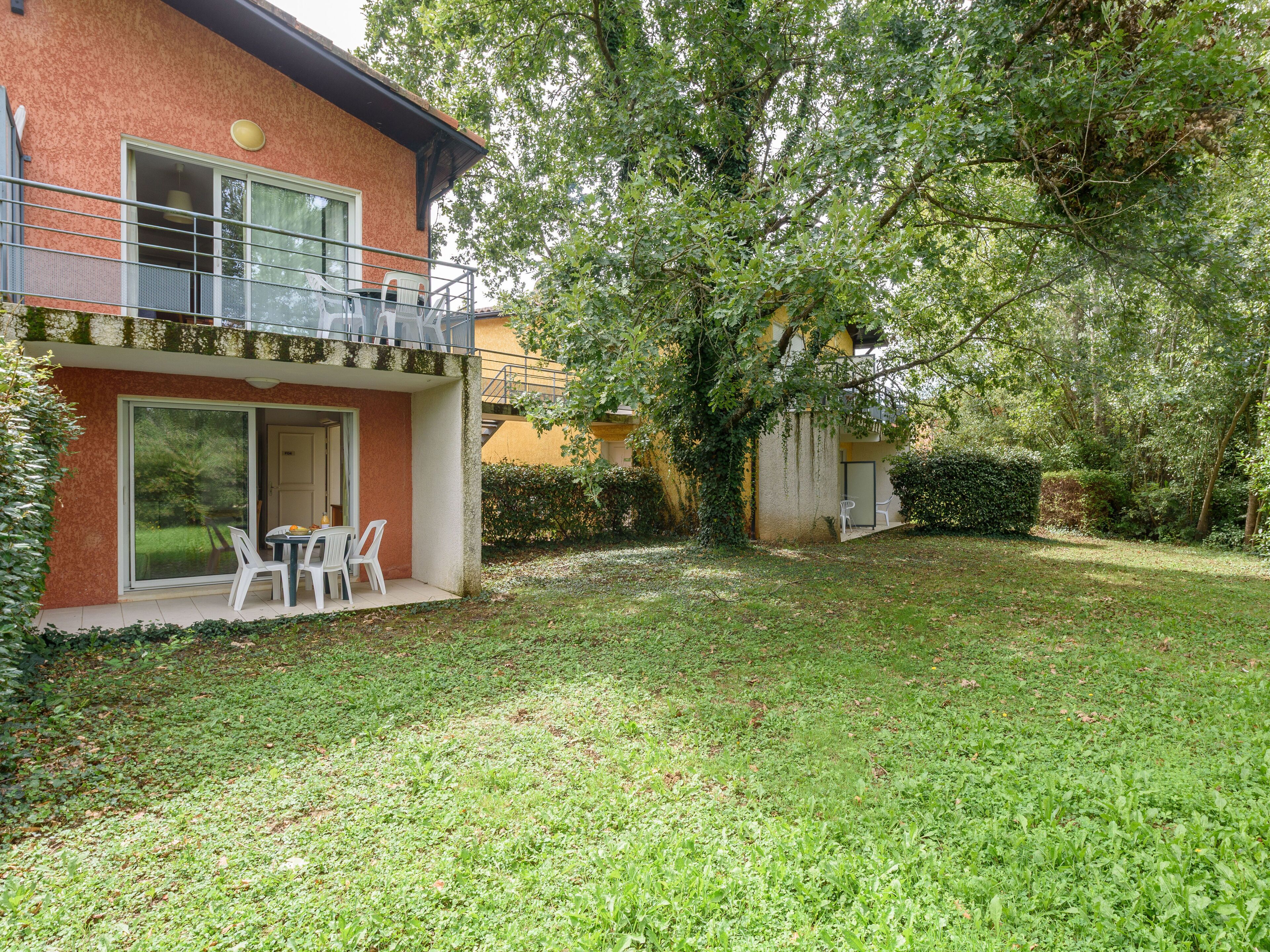A modern building with a balcony, a small patio with chairs, and a well-maintained lawn.