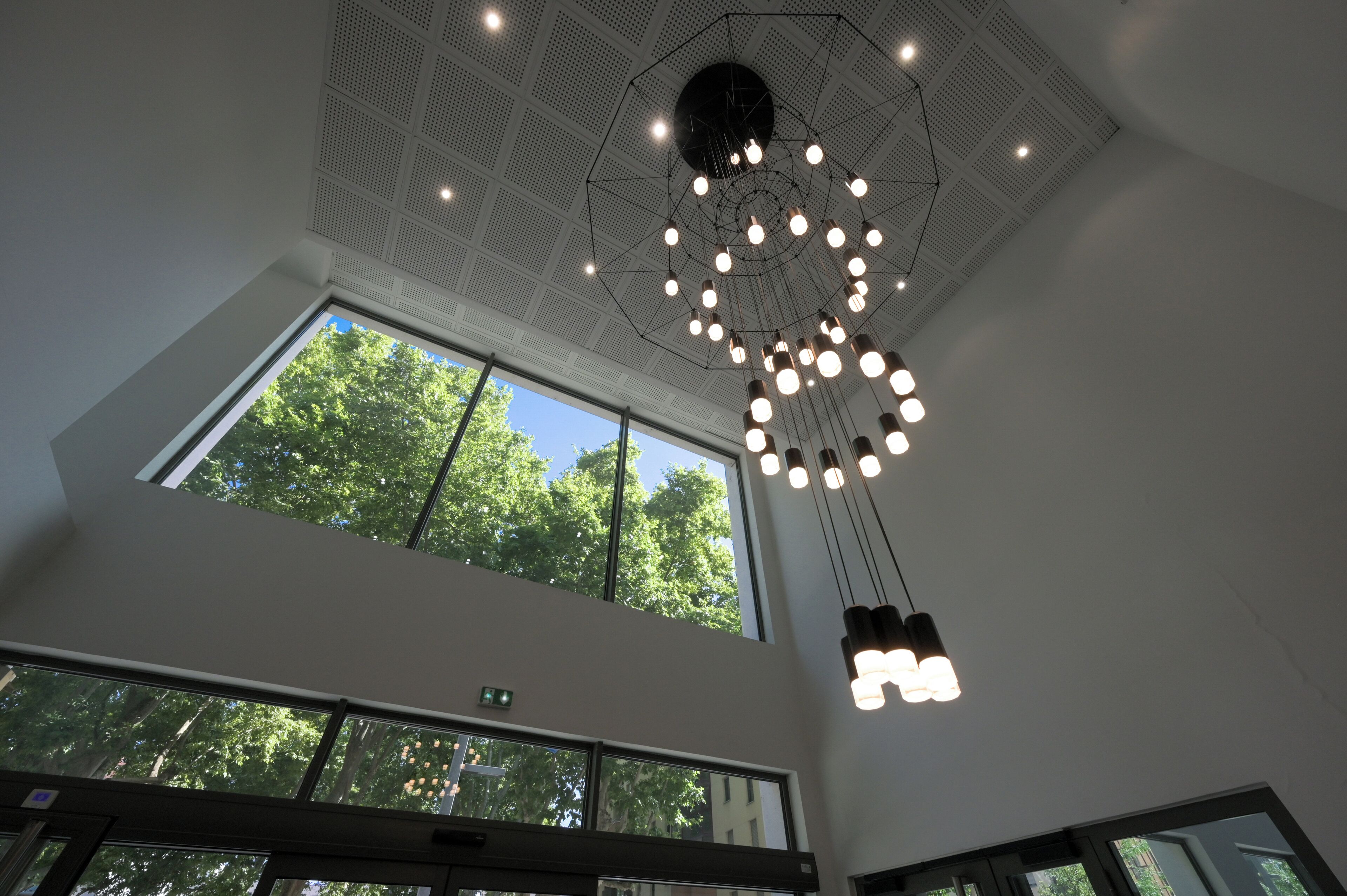 A modern interior with a high ceiling, large windows, and a unique geometric light fixture.
