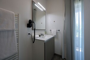 Un baño con lavamanos blanco, espejo, toallero y ducha.