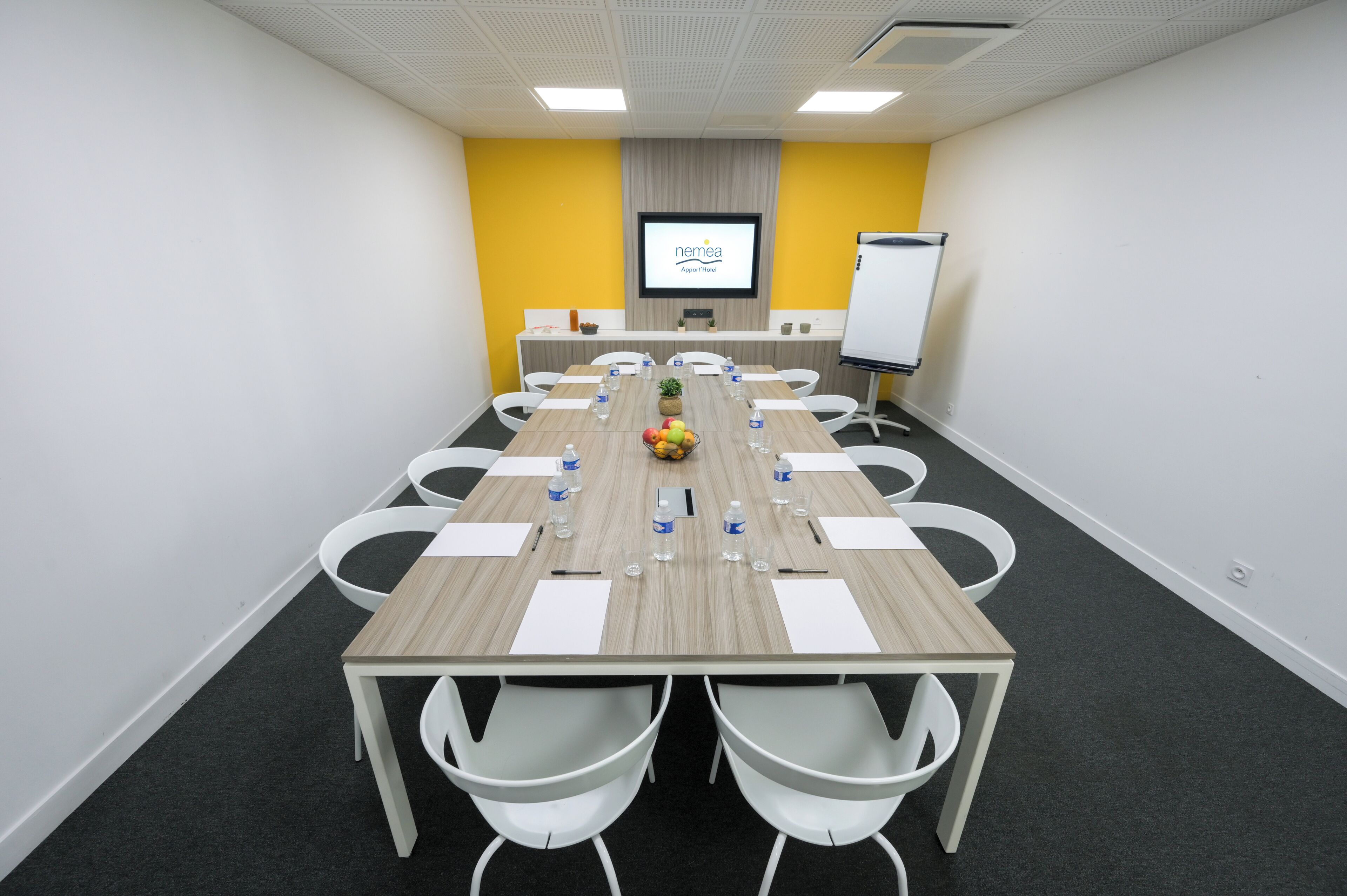 A conference room with a long table, white chairs, water bottles, and a whiteboard.
