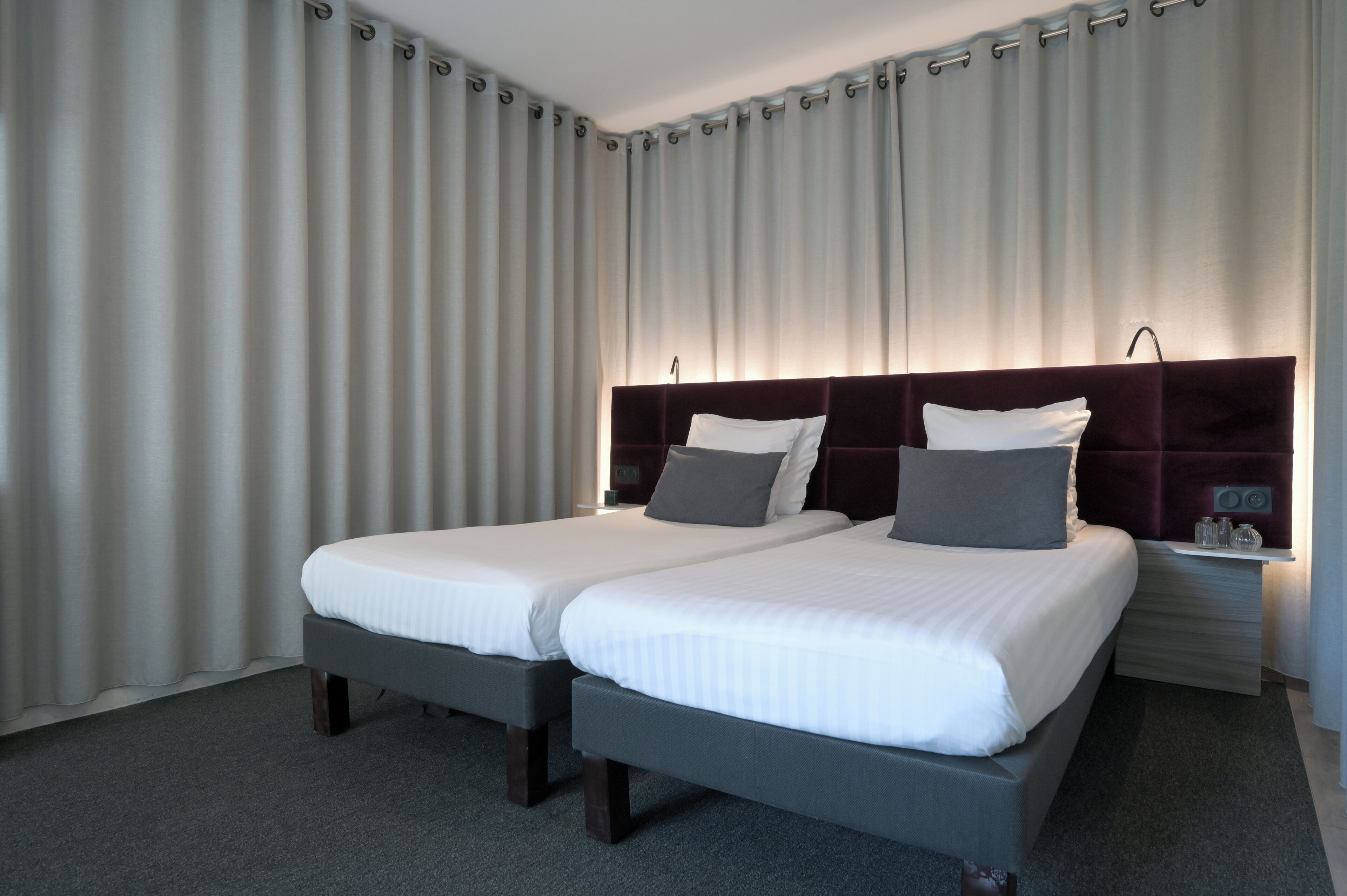 A hotel room with two beds, a dark headboard, and a nightstand with a lamp.