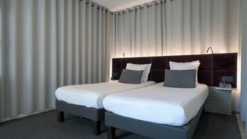 A hotel room with two beds, a dark headboard, and a nightstand with a lamp.