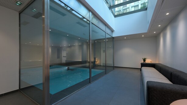 A modern indoor swimming pool with glass walls, a skylight, and a minimalist design. - Nemea Appart Hotel So Cloud Lyon Part Dieu (Lyon)