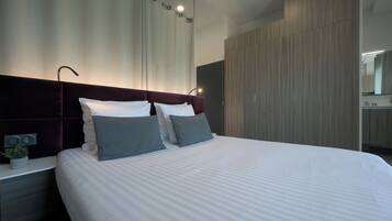 Una habitación de hotel moderna con una cama grande, una mesita de noche, una planta en maceta y un armario de madera.